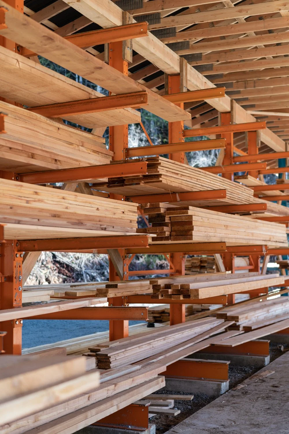 Stacks of lumber waiting at a construction site with steel supports and a wooden roof overhead.