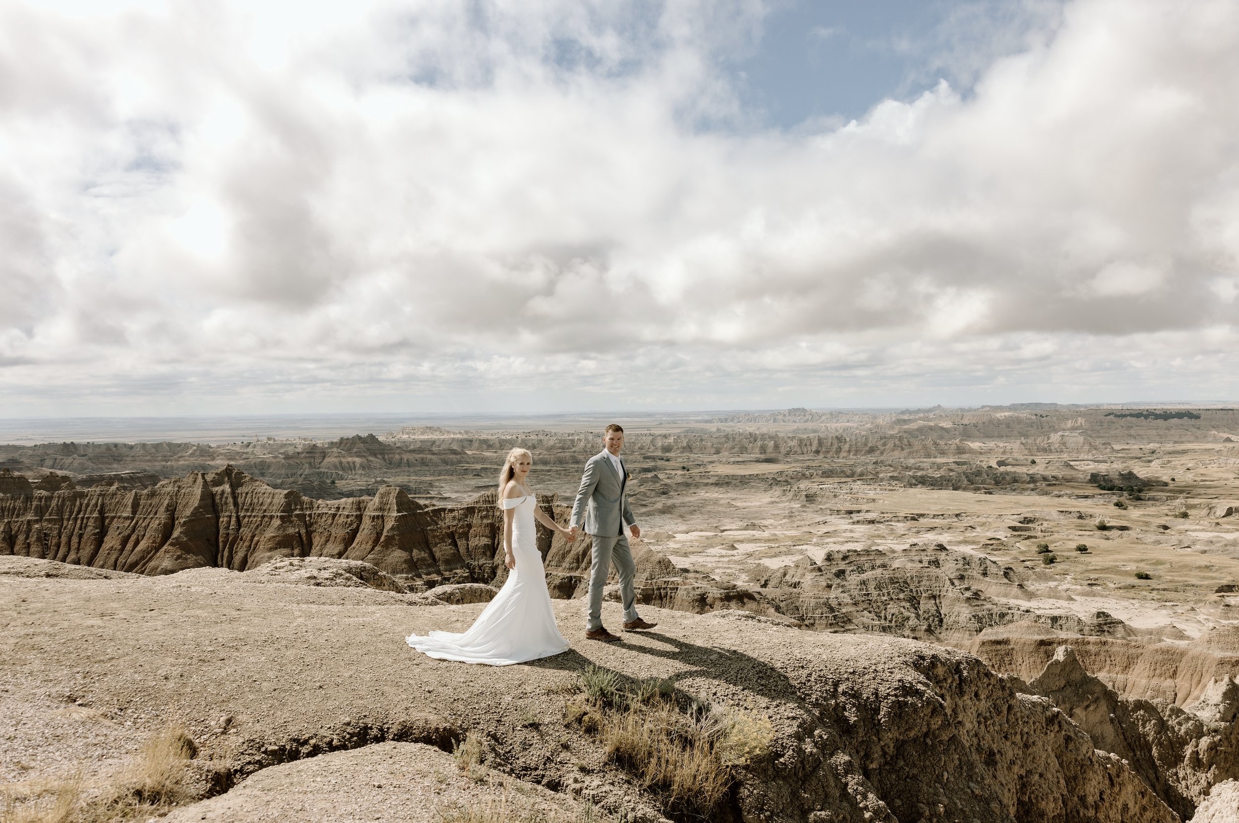 A bride and groom holding hands and walking in the Grand Canyon on a cloudy day.