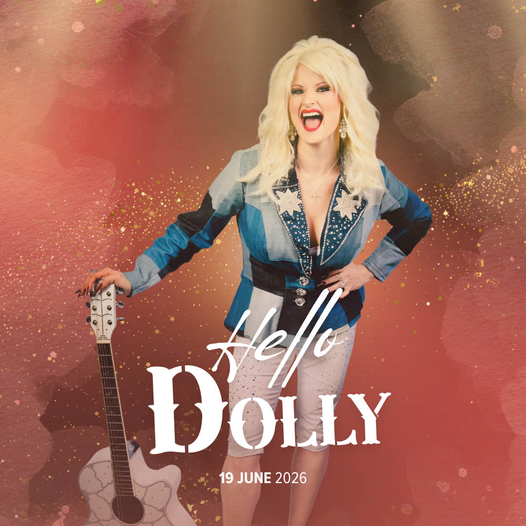 A woman with platinum blonde hair styled in voluminous layers, wearing a colorful patchwork jacket, white shorts, and earrings, standing against a pink and gold splattered background, holding a white acoustic guitar, smiling and shouting.