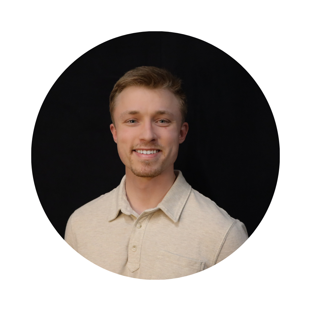 A young man with light brown hair, smiling, wearing a beige polo shirt, against a dark background.
