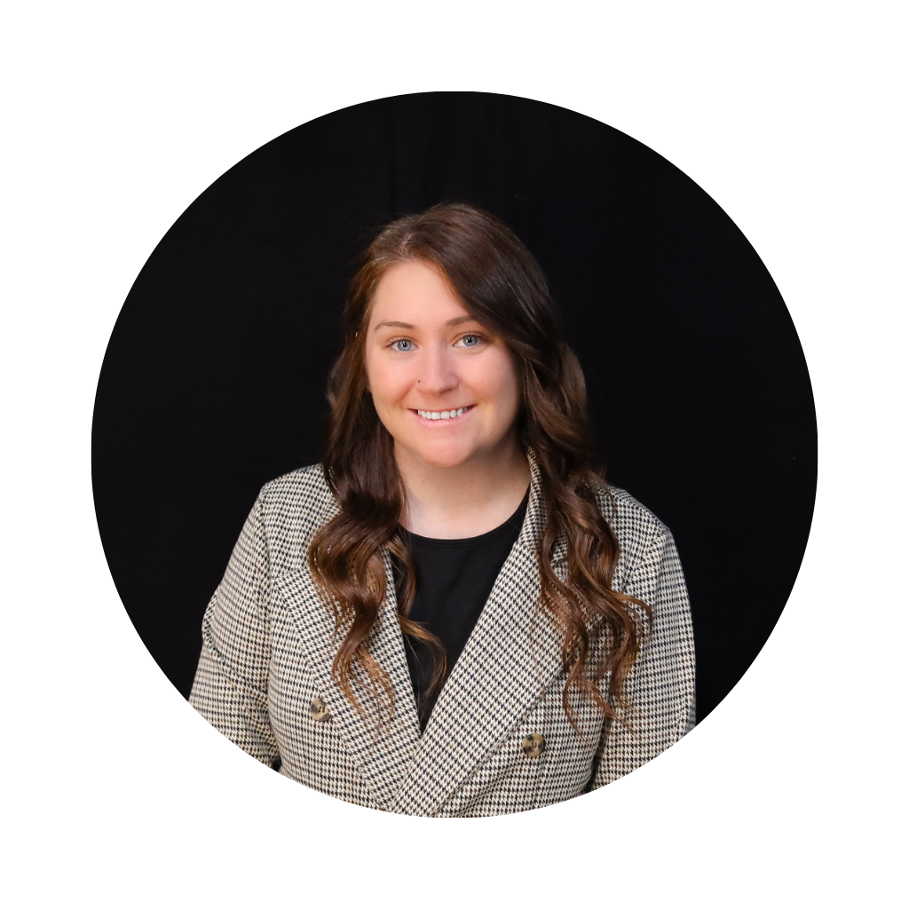 Portrait of a smiling woman with long brown wavy hair, wearing a houndstooth blazer and black top, against a black background.