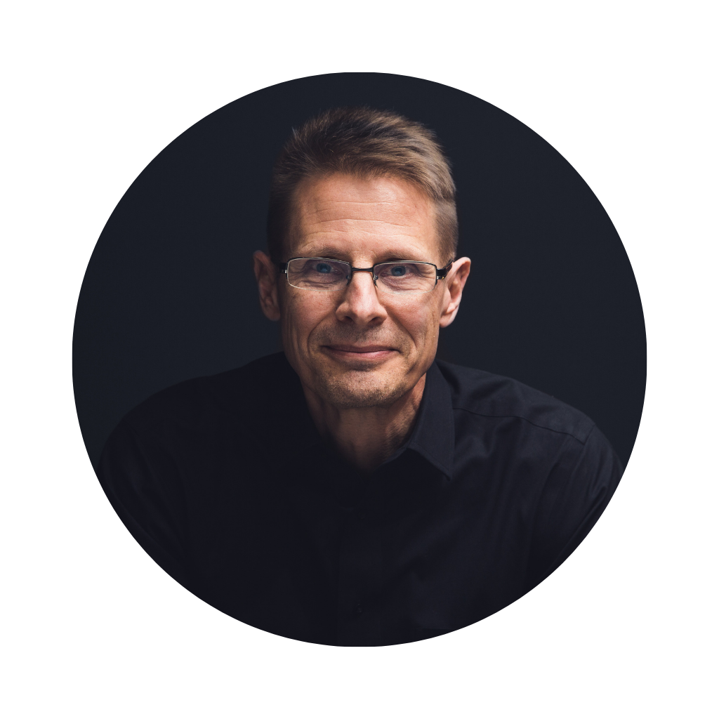 A middle-aged man with glasses and short brown hair, wearing a black shirt, appears against a dark background.