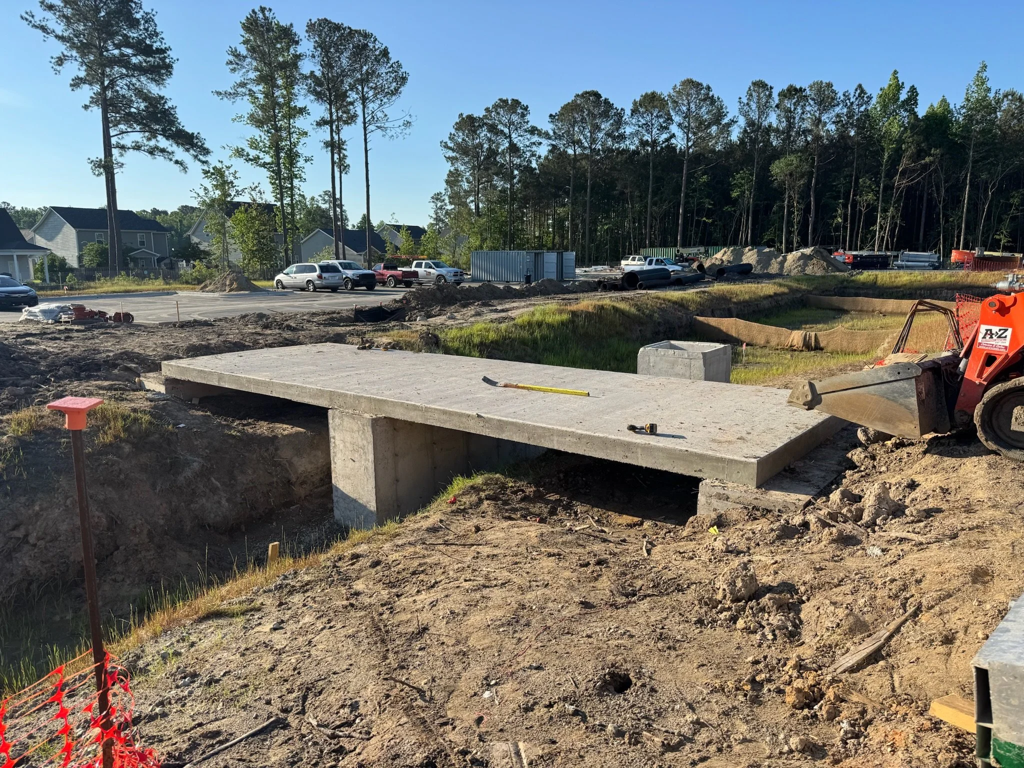 Construction site with a metal beam supported by a concrete pillar, surrounded by gravel and dirt, with a partially constructed roof overhead.