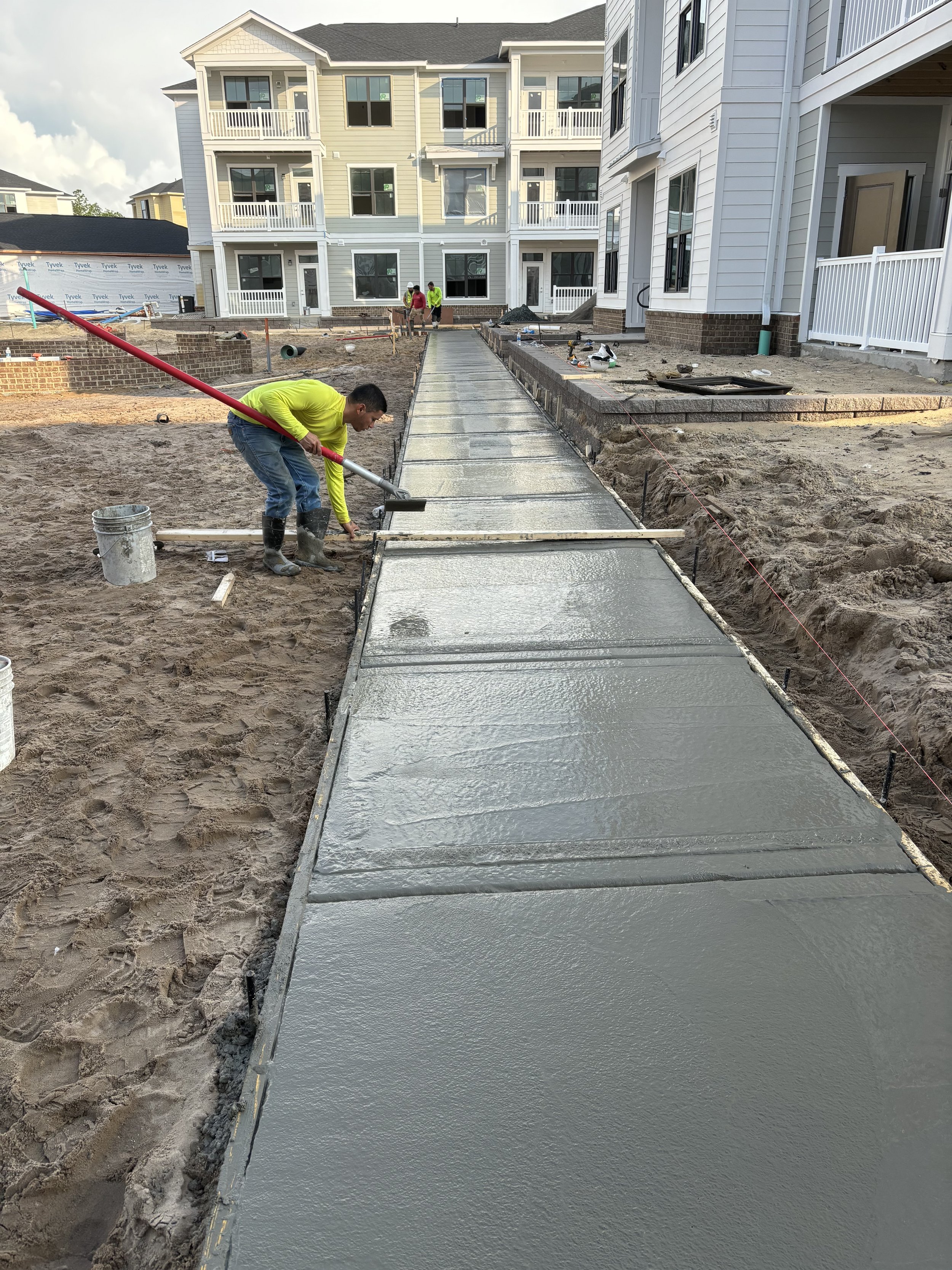 Construction workers smoothing wet concrete on a sidewalk outside a building with stone facade and glass doors.