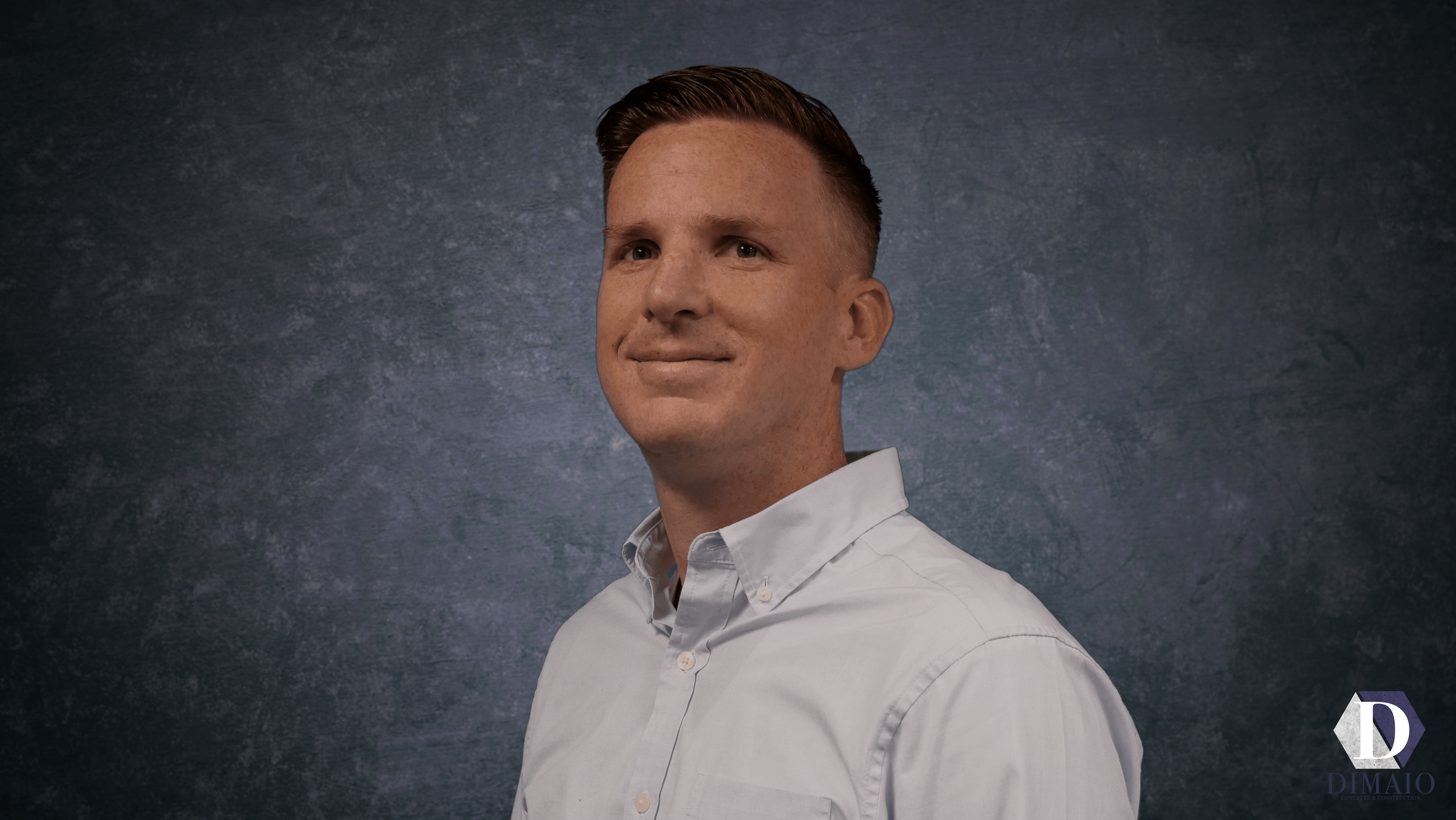 A man with light skin, short brown hair, wearing a white button-up shirt, looking slightly to the side against a dark textured background.