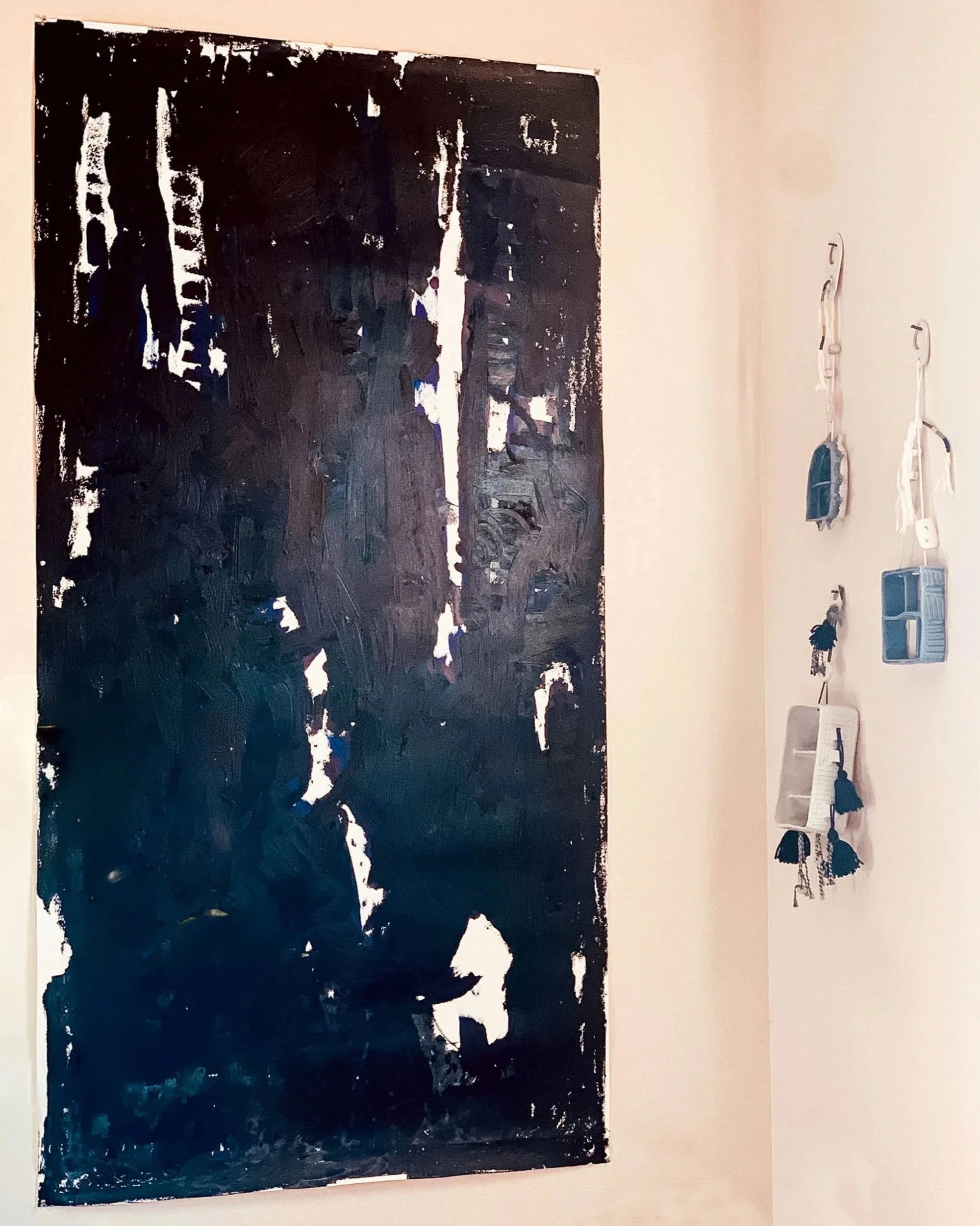 Abstract black and white painting on a wall with some hanging keychains and small storage containers to the right.