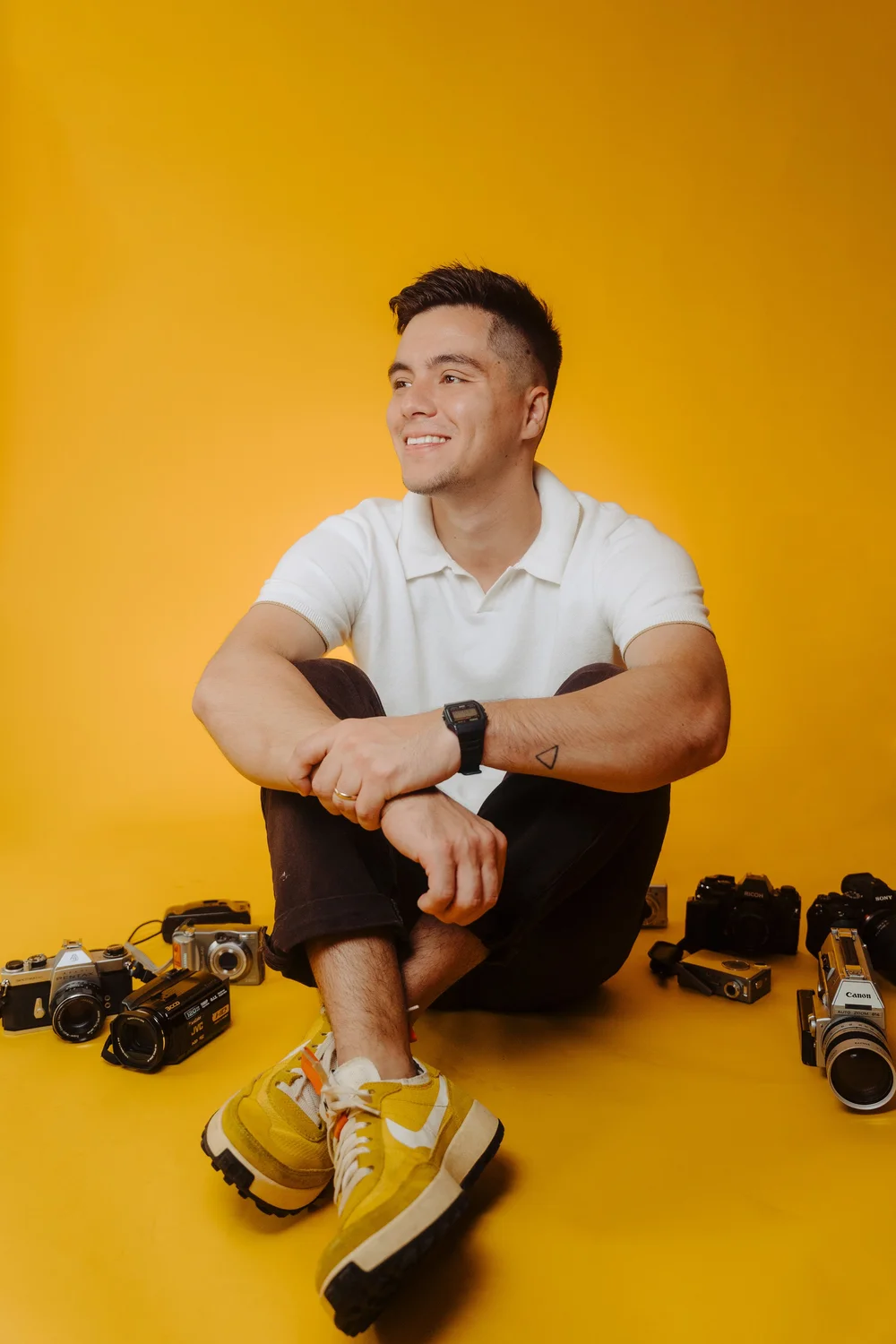 Nate Bustamante of NB Films sitting with his cameras on a mustard backdrop