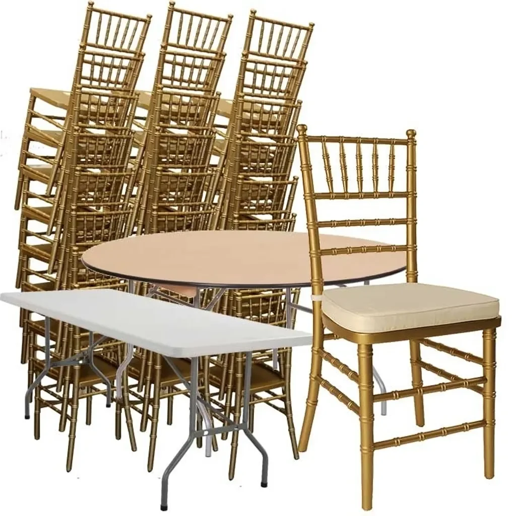 Multiple gold-colored banquet chairs stacked behind a round table and a white portable table, with one gold chair in front.