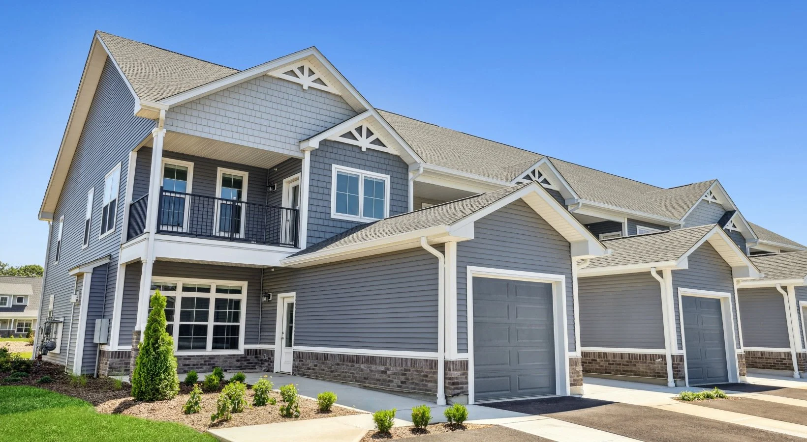 A row of modern two-story townhouses with gray siding, white trim, and attached garages under a clear blue sky.