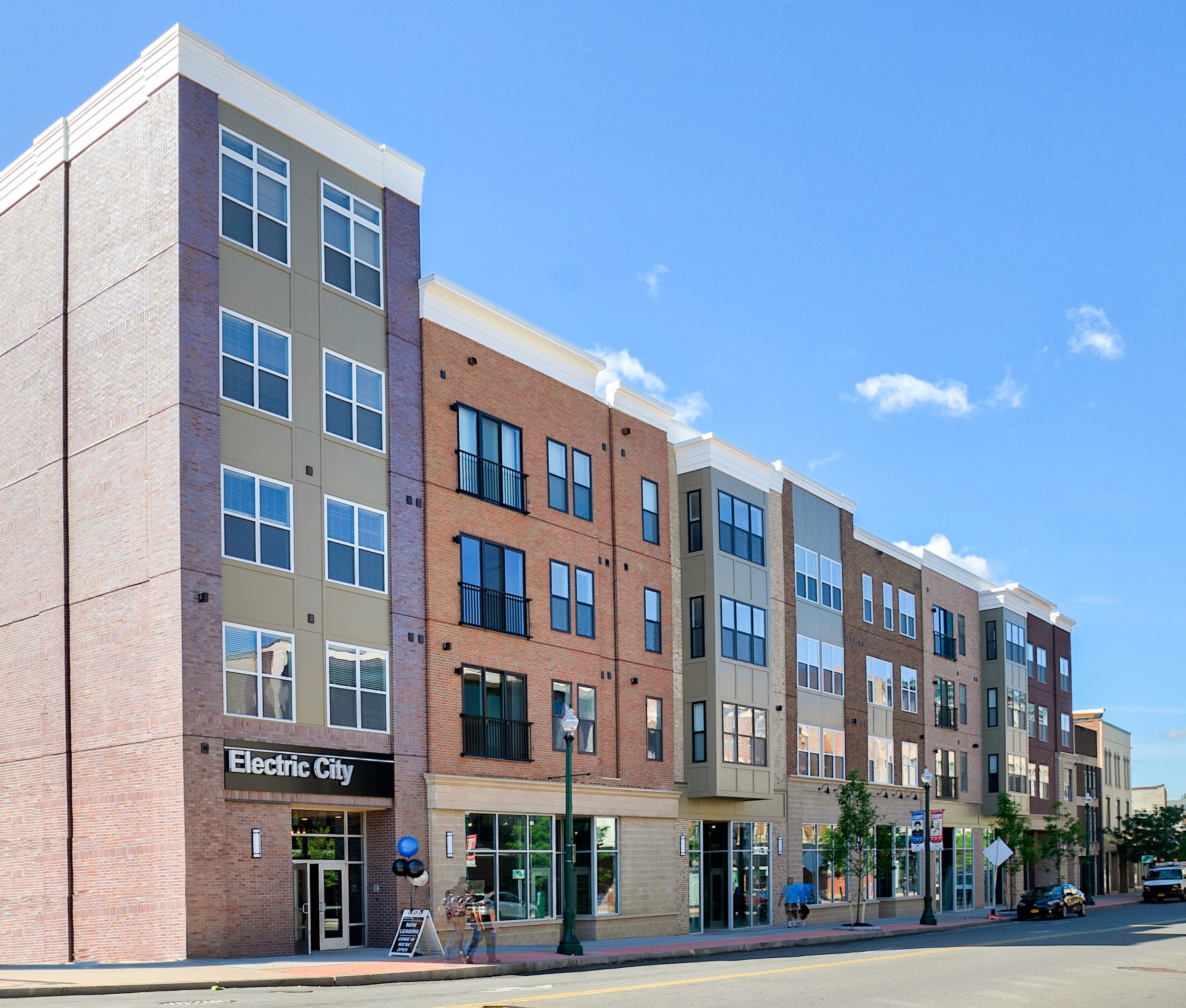 Modern multi-story residential and commercial building with colorful brick and panel facades on a city street under a blue sky.