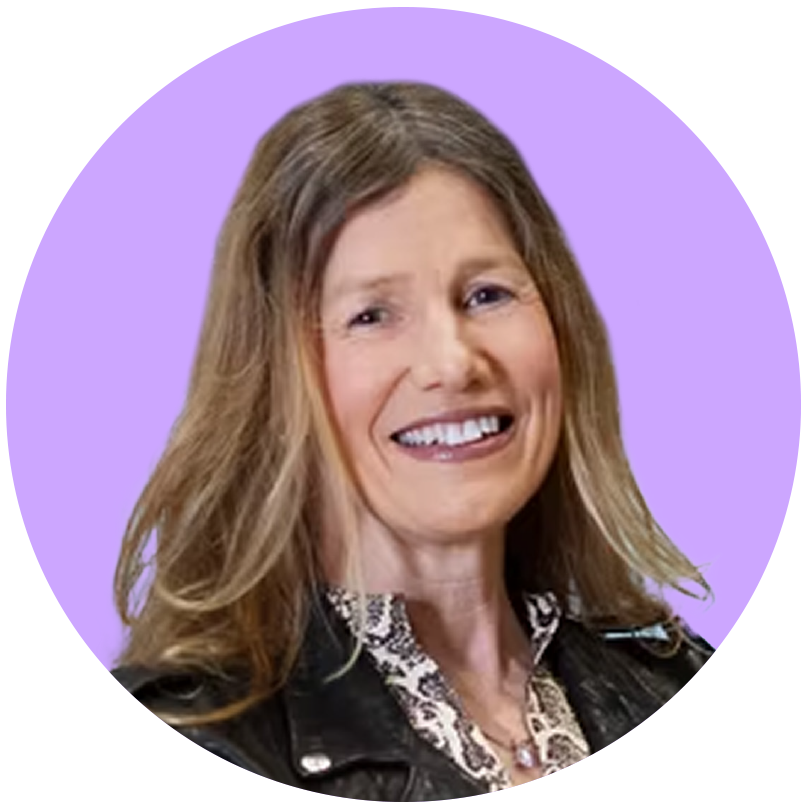 A woman with light brown hair smiling, wearing a black leather jacket and a patterned blouse, with a purple background.