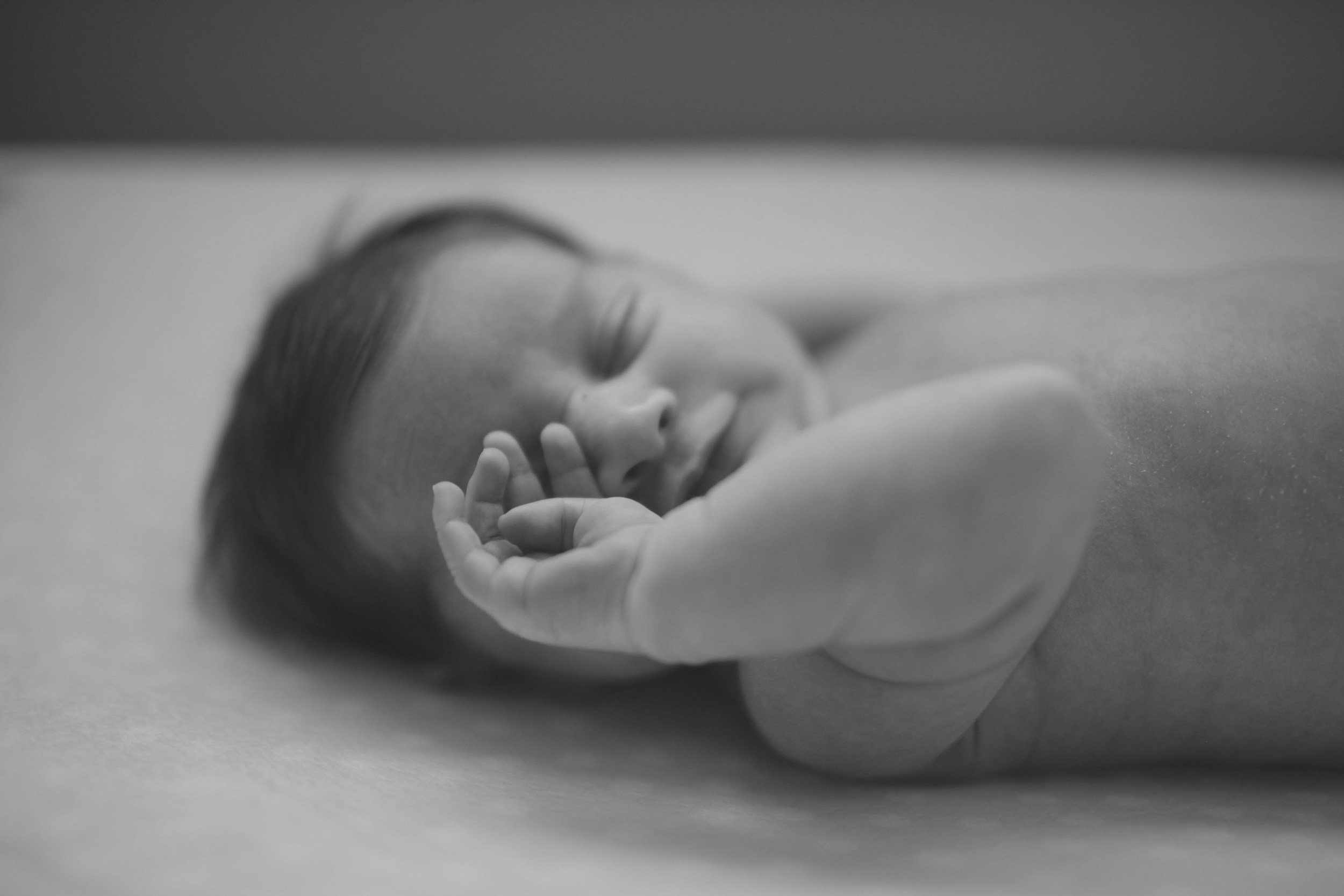 Close-up black and white photo of sleeping newborn baby with hands raised