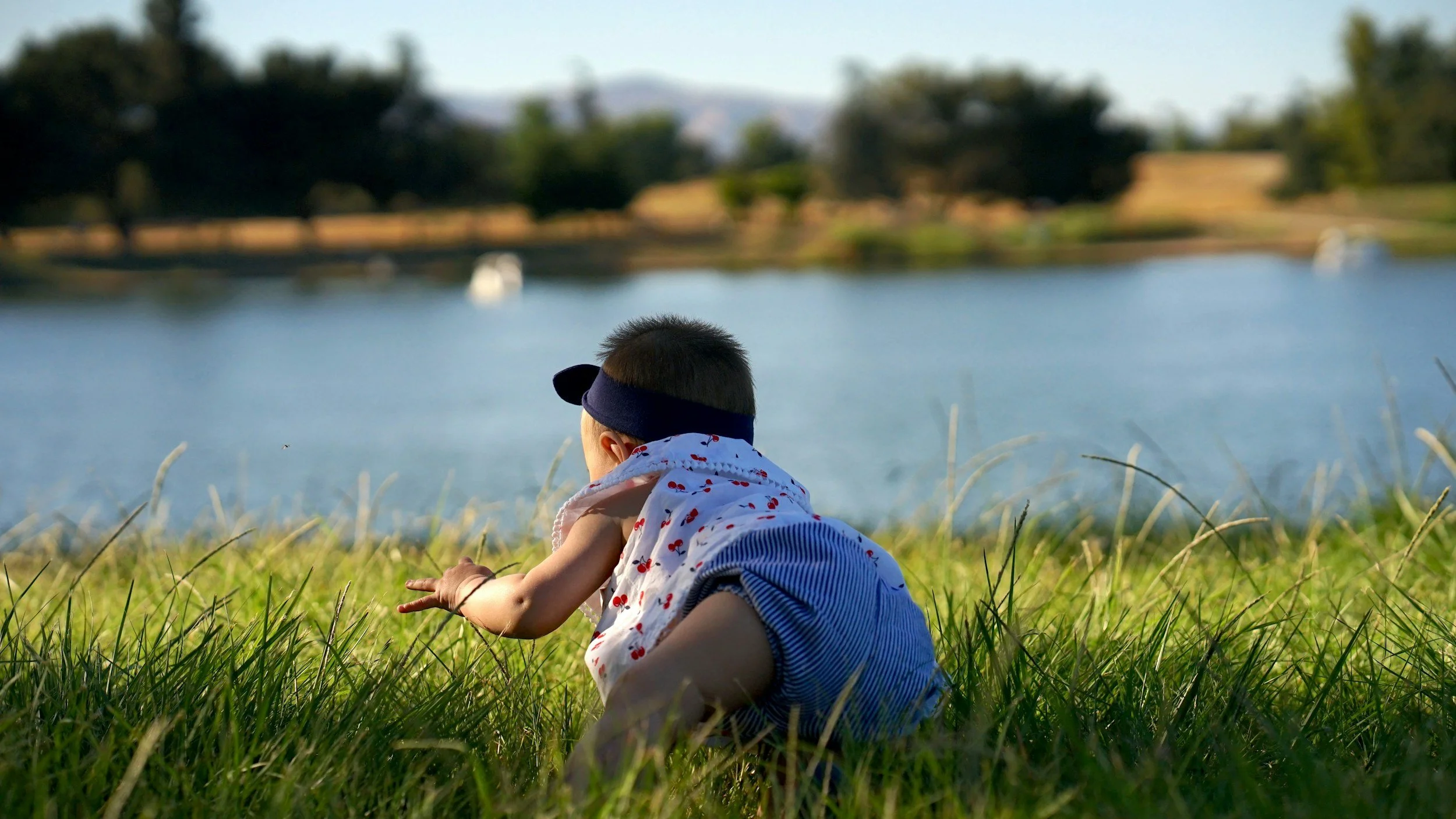 Baby crawling on grass outdoors by a lake on a sunny day