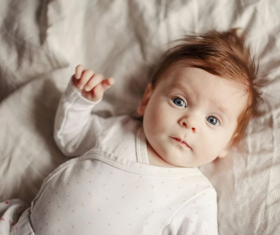 Alert baby lying awake on a bed, wide-eyed instead of settling to sleep
