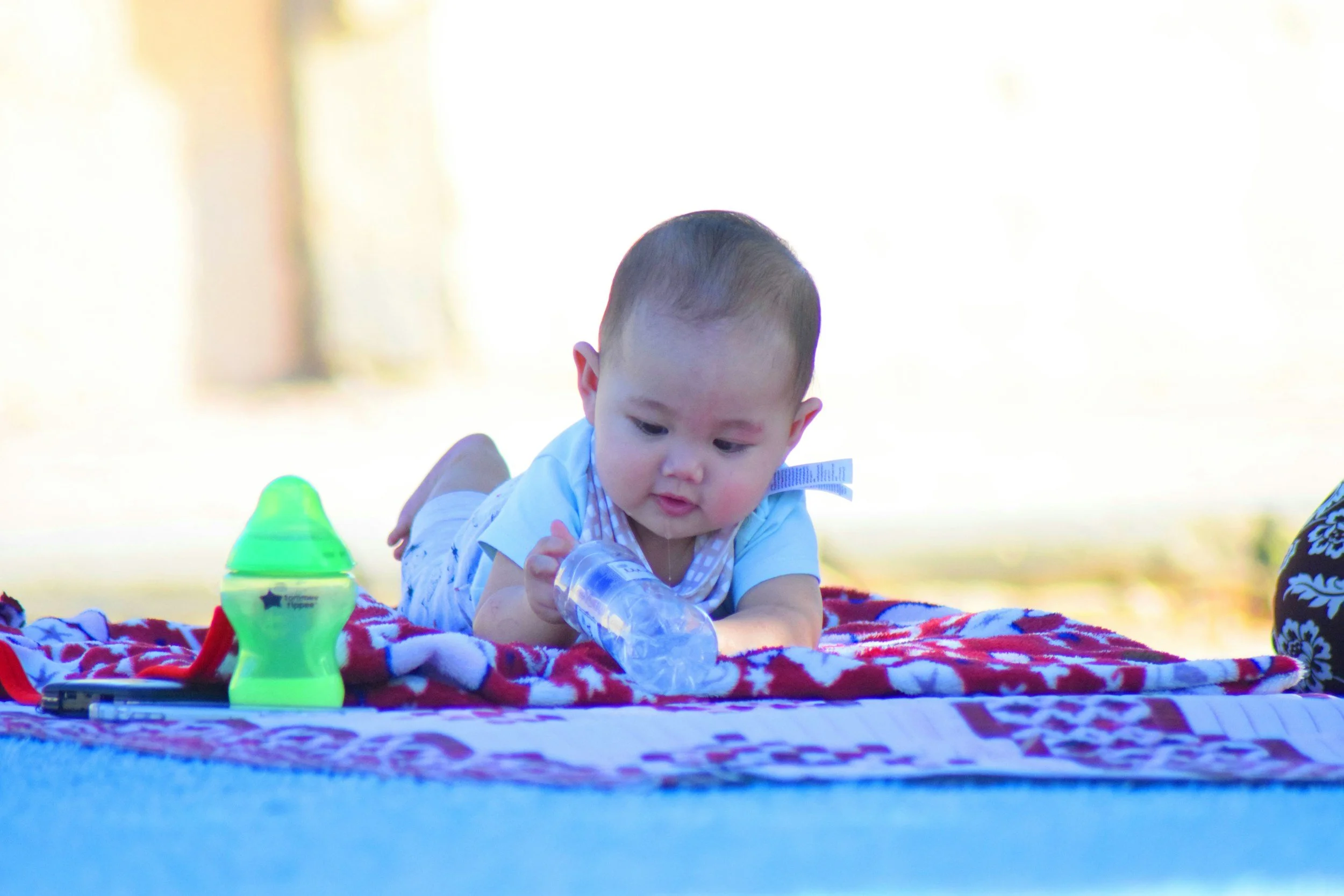 Baby lying on stomach on blanket playing with a plastic water bottle