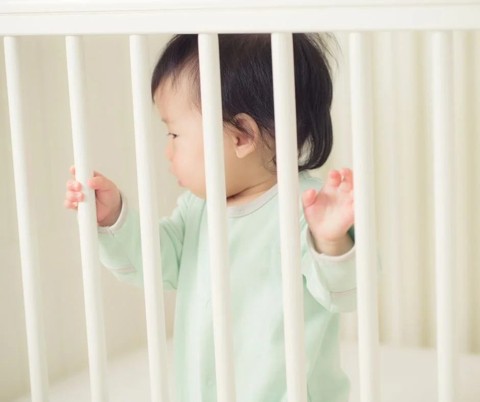 Baby standing up in cot holding the bars during a developmental leap that can cause false starts at bedtime