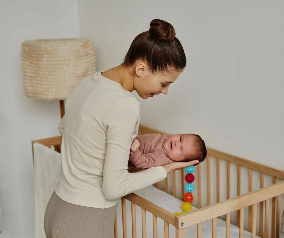 Mother gently lowering sleeping baby into cot at bedtime