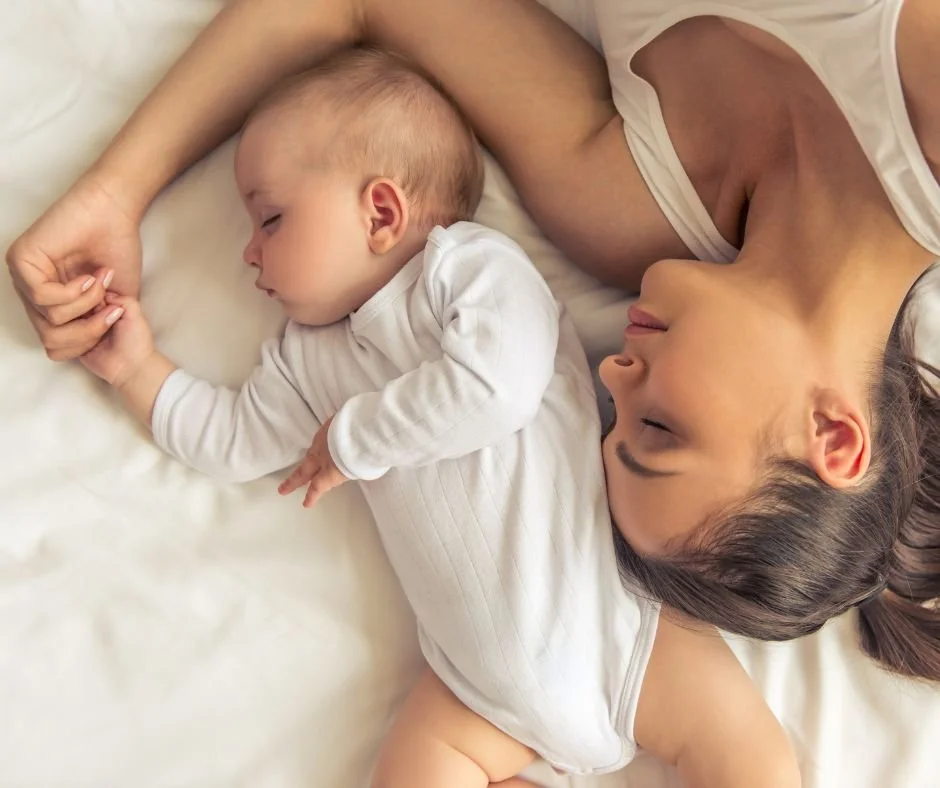 Mother and baby lying face to face in bed, holding hands