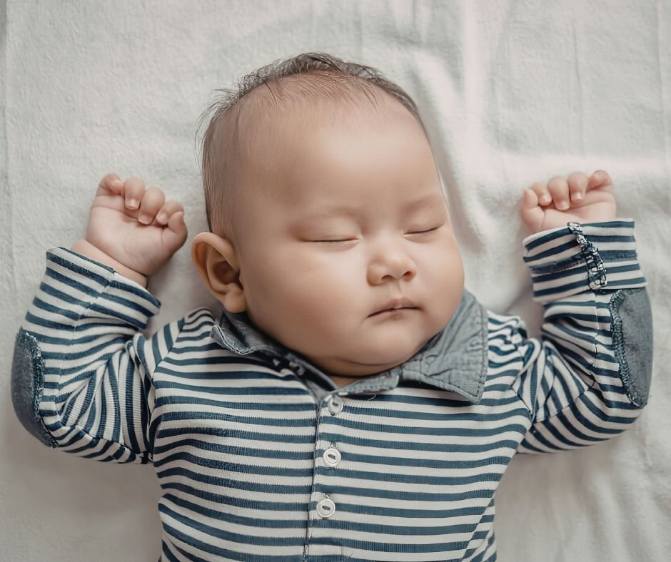 A sleeping baby lying peacefully with arms stretched above their head