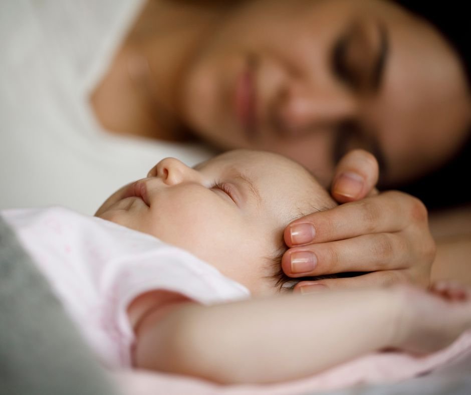 Mother lying in bed cradling her sleeping baby's head