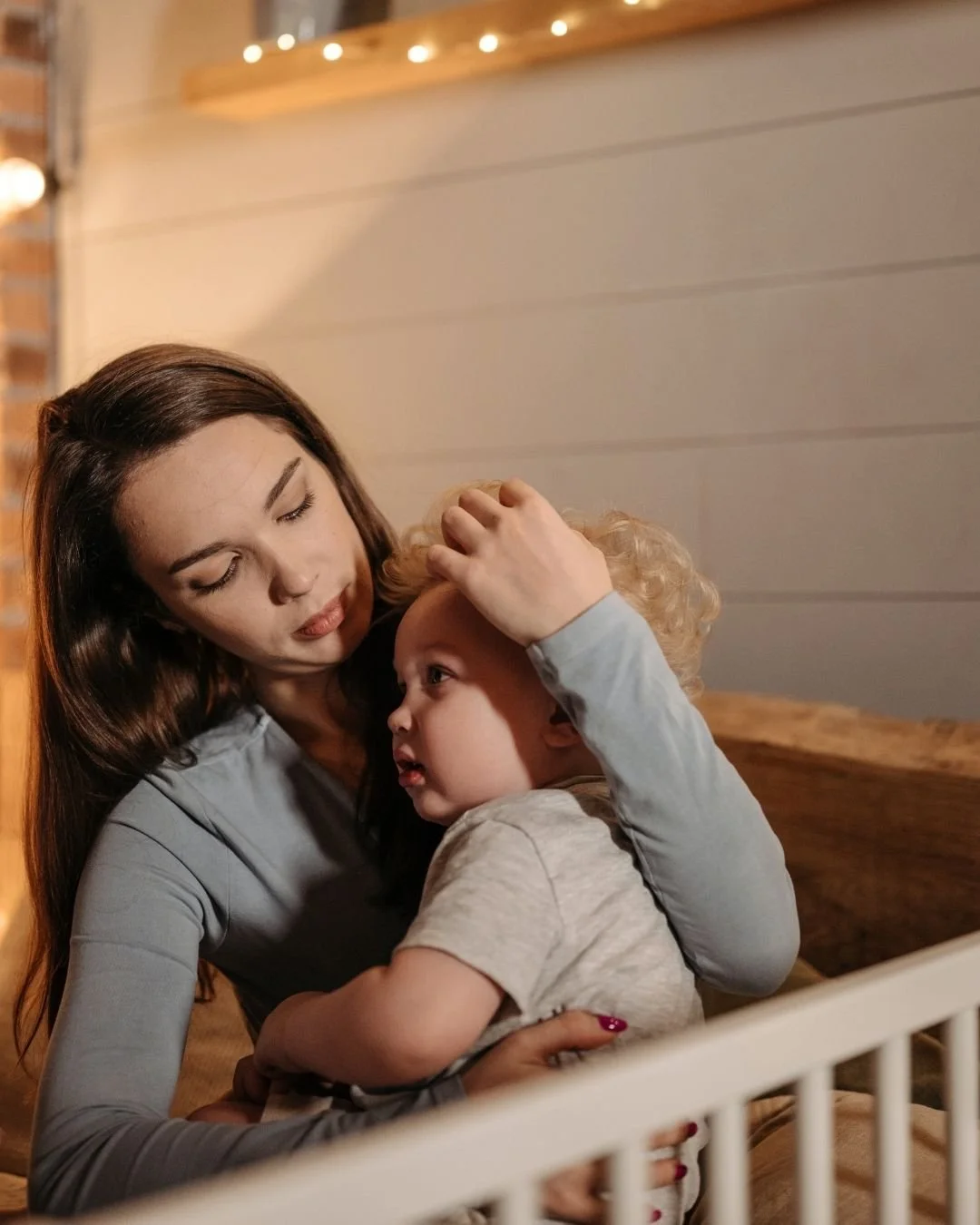Parent gently soothing a toddler by a cot during bedtime wind-down