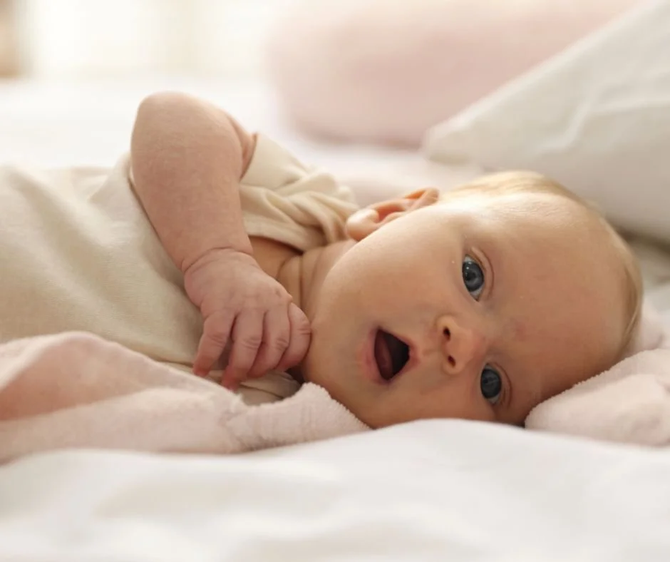 Wide awake baby lying on side with mouth open staring at camera