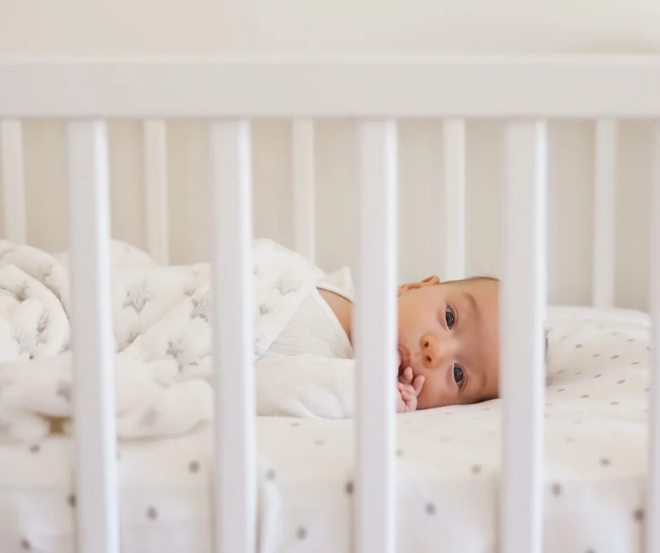 Wide awake baby lying in cot staring through cot bars