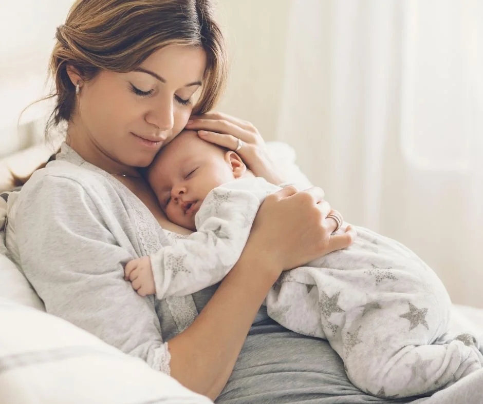 Calm looking mum holding her sleeping baby up against her chest with her face against baby's head and her hand on baby's head.