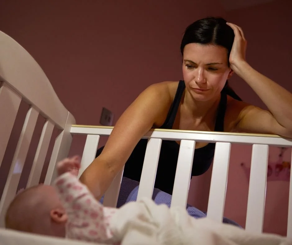 Exhausted mother leaning over cot at night after baby wakes with a false start at bedtime