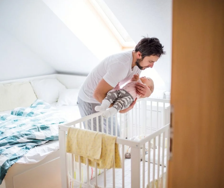 Parent gently placing sleeping baby into cot during nap transition