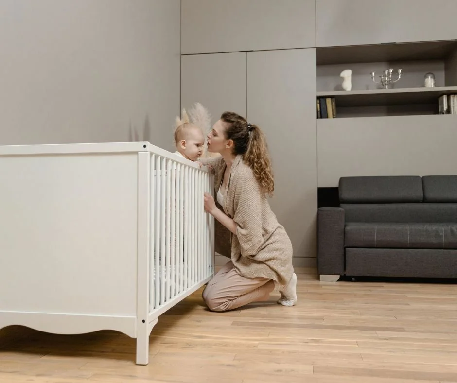 A baby in their cot with their mother sitting close by, offering reassurance during the room move