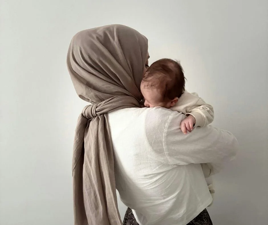 Mum wearing a beige hijab holding a baby snuggling into her shoulder