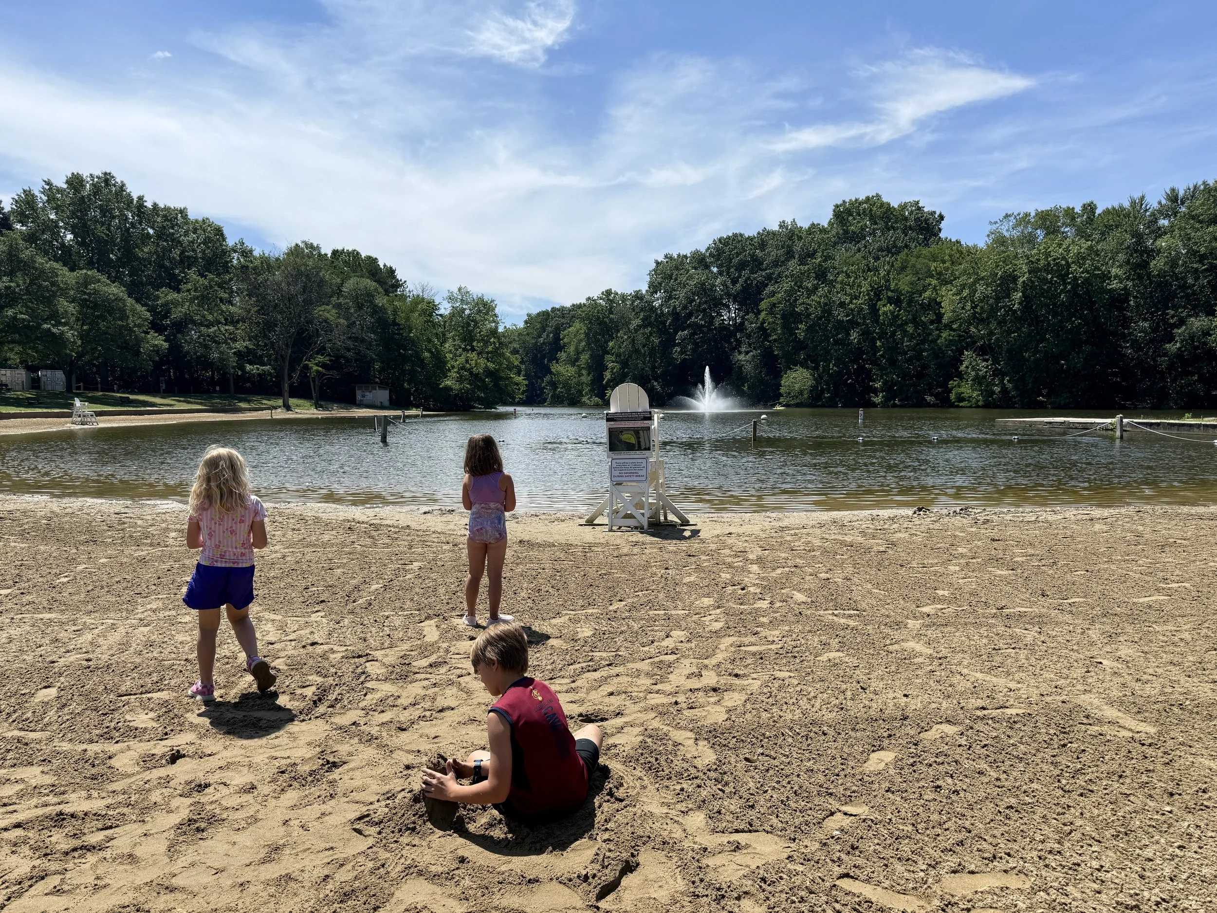 picture of kids playing on a beach with a fountain in the middle of the lake