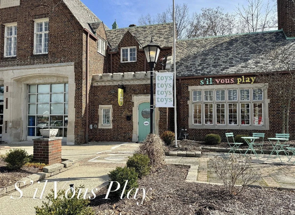 Beautiful brick building with a teal door and colorful sign that reads S'il Vous Play Toys