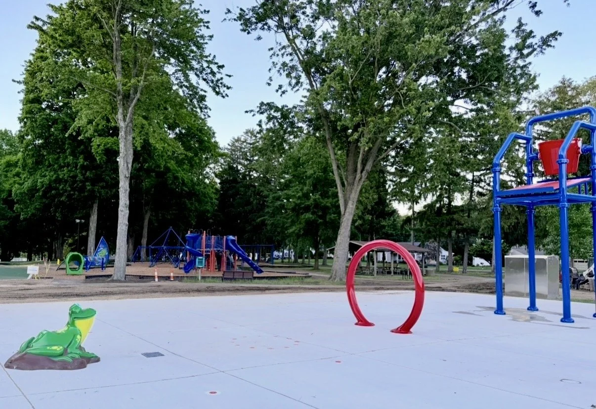 splash pad with a frog and large bucket and a playground in the background