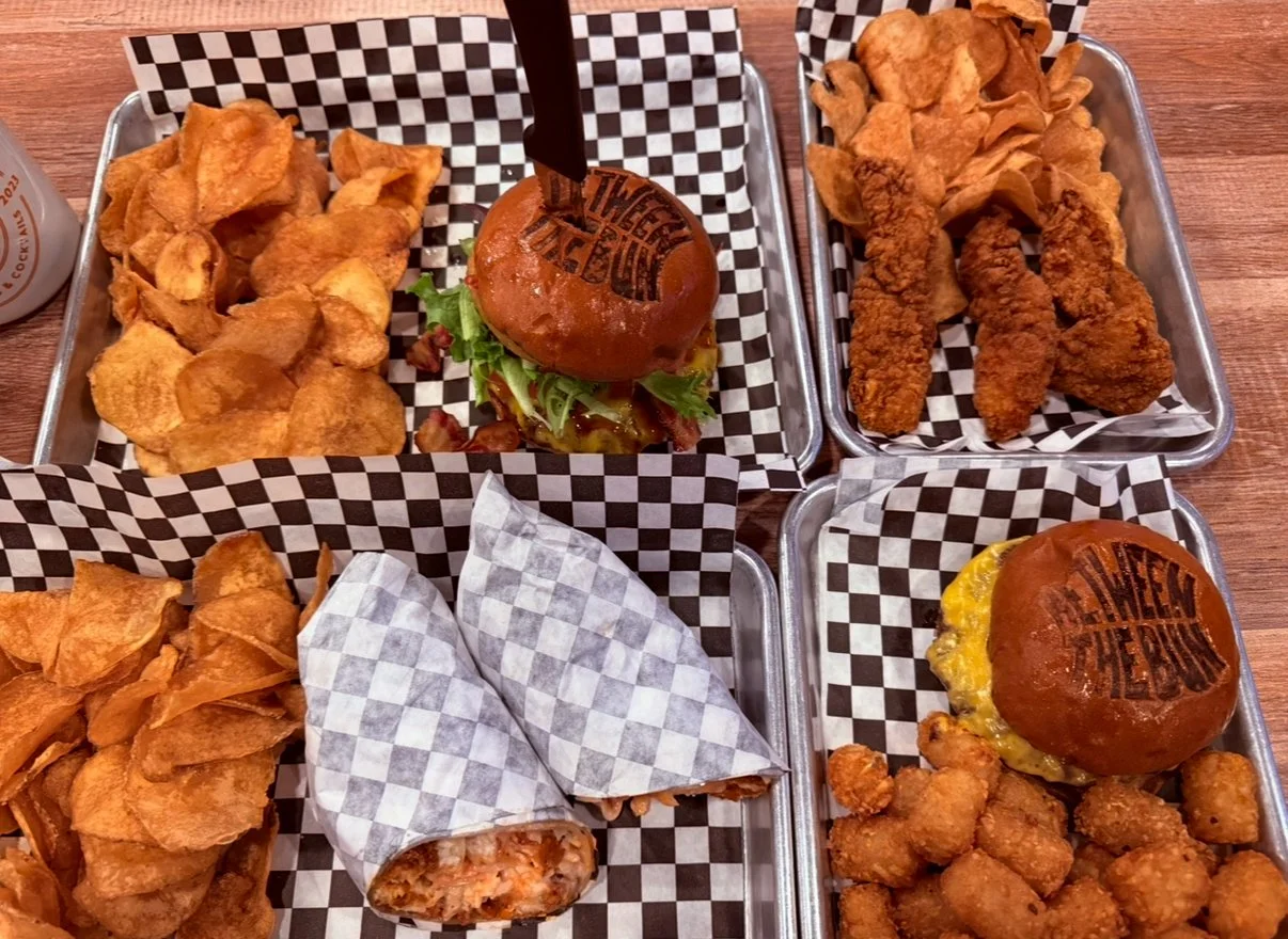 four trays of food with burgers, chicken strips, chicken wrap and house chips