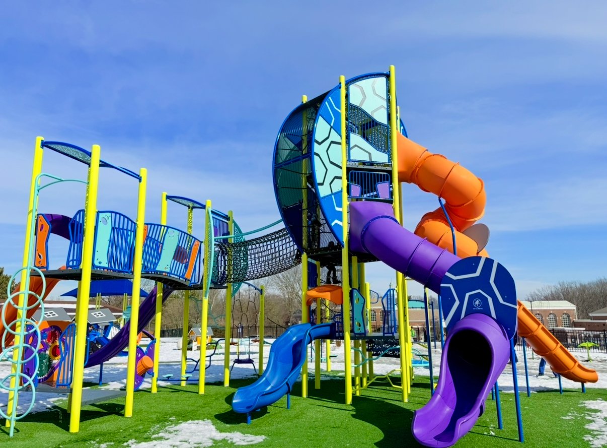 large colorful playground structure with tall curly slides and a net to crawl through.