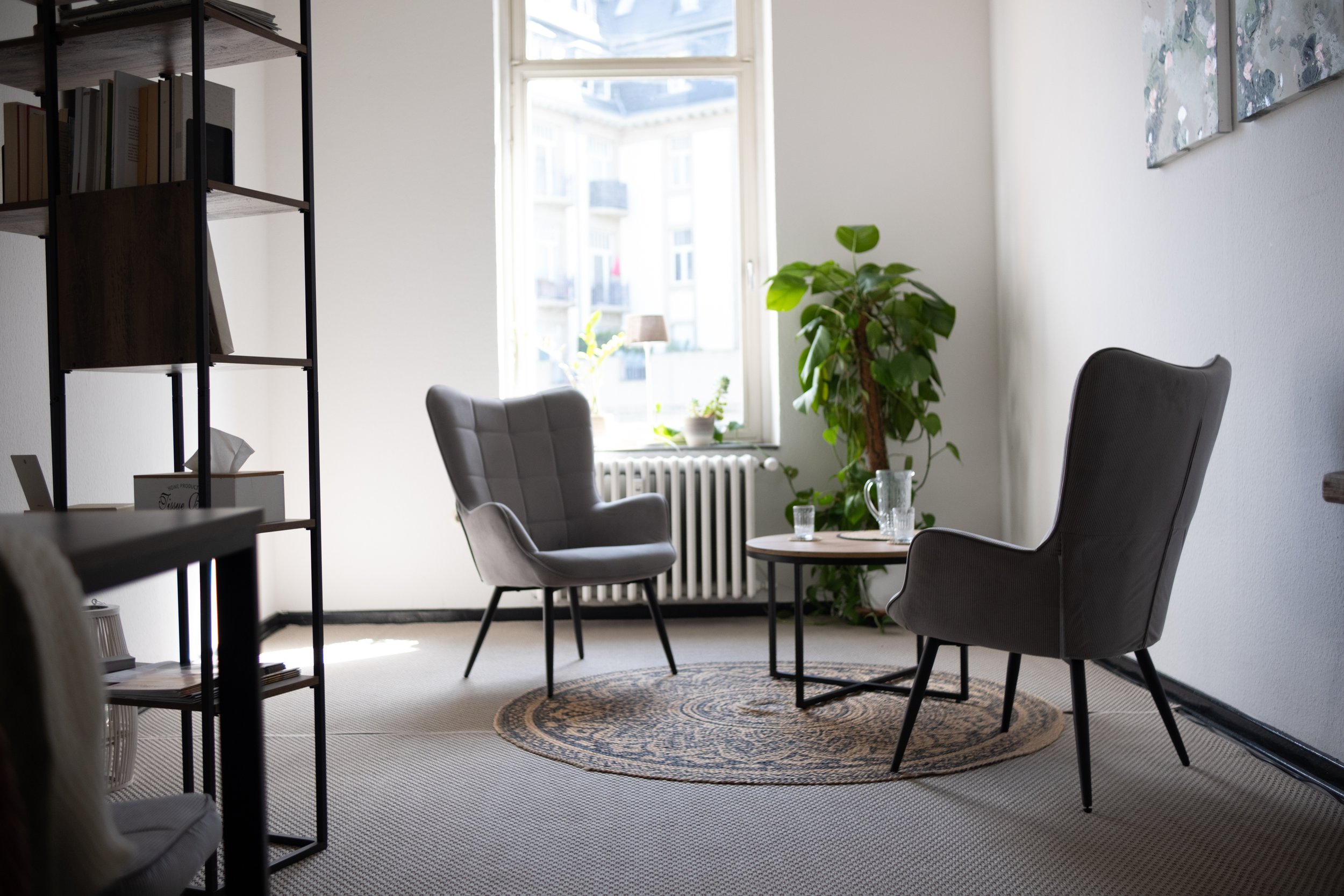 Leeres Raumkonzept im Herzen Bad Nauheims zur Miete. Man sihet zwei gemütliche Sessel und einen Teppich, ein Regal. 