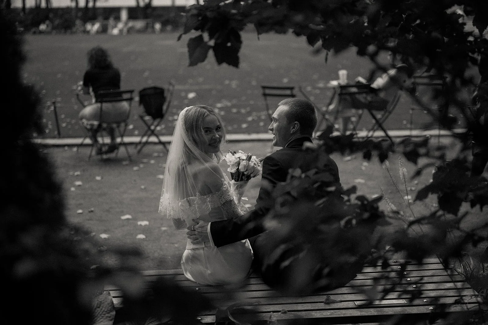 Couple seen through the trees on a bench in Bryant park before their Cakewalk elopement ceremony.