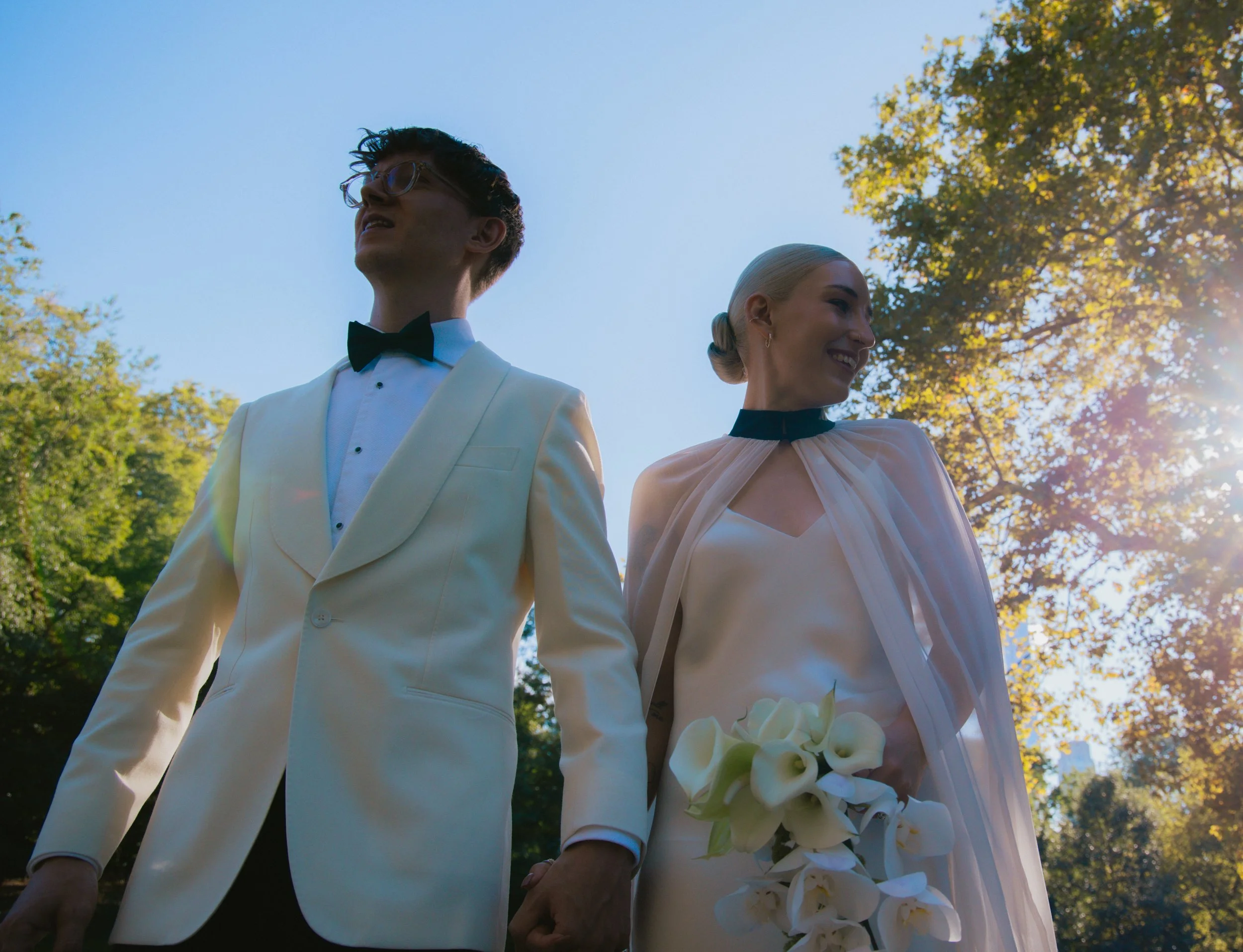 Bride and groom walking through Central Park with the sky and trees above them after their elopement ceremony.