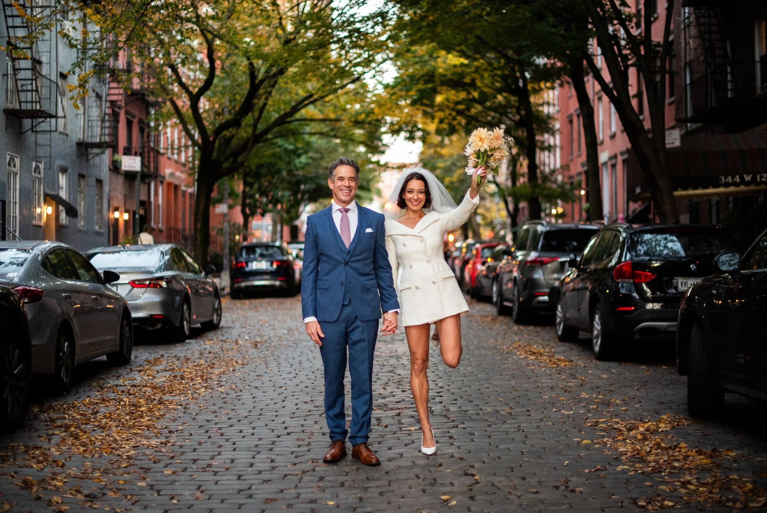Couple jumping on a cobblestone street during their NYC elopement in fall, photographed by Cakewalk
