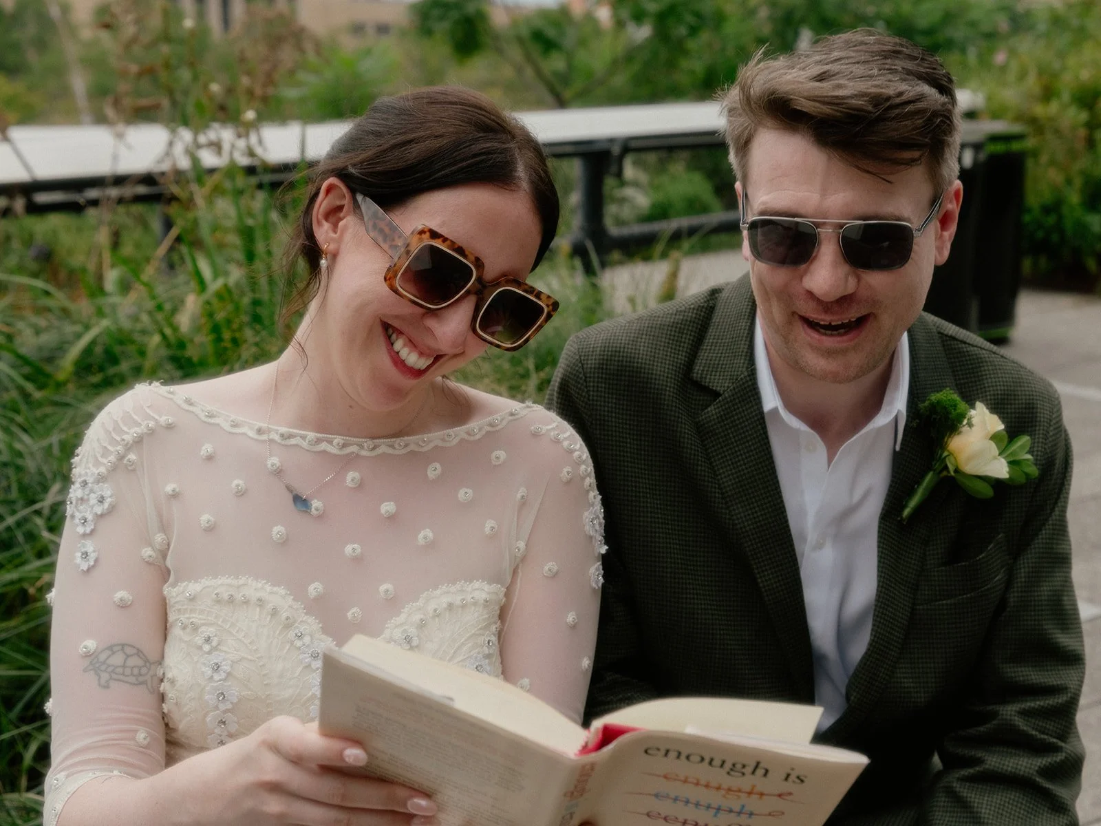 Bride and groom smiling and reading from a book, seated on a bench on New York's High Line.