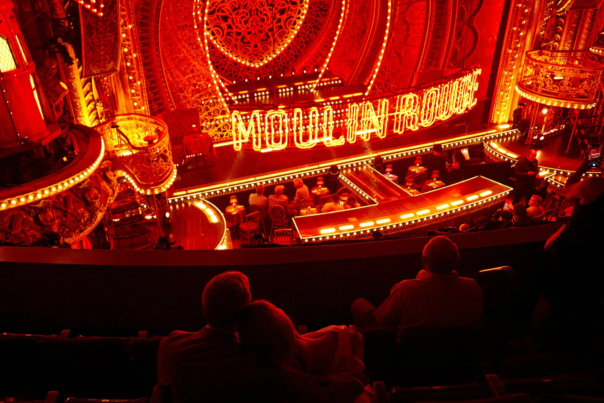 Bride and groom leaning on each other in the balcony of a theatre where Moulin Rouge! is about to be performed on Broadway.