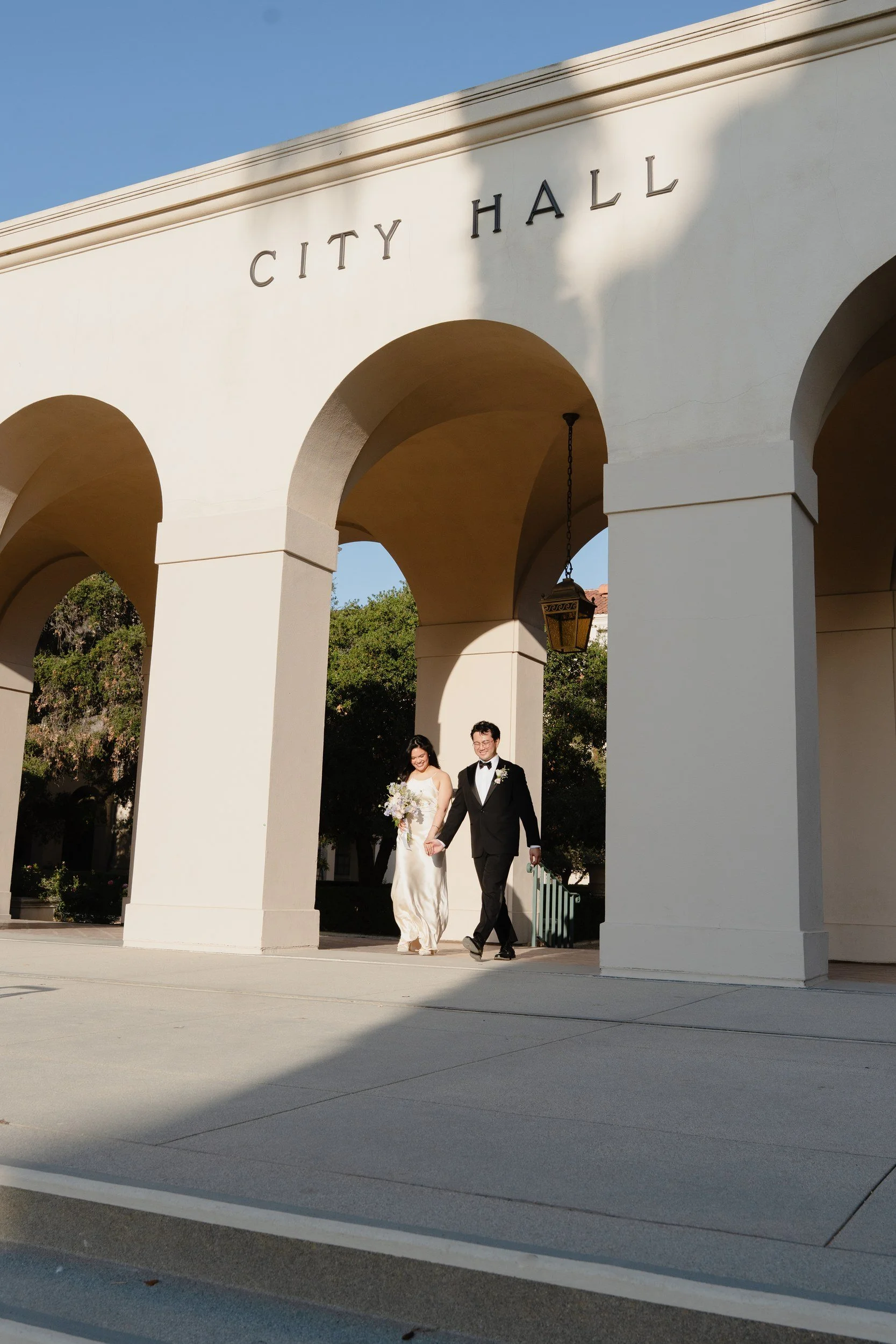 Couple walking out through the arches at their sunrise Pasadena City Hall elopement.