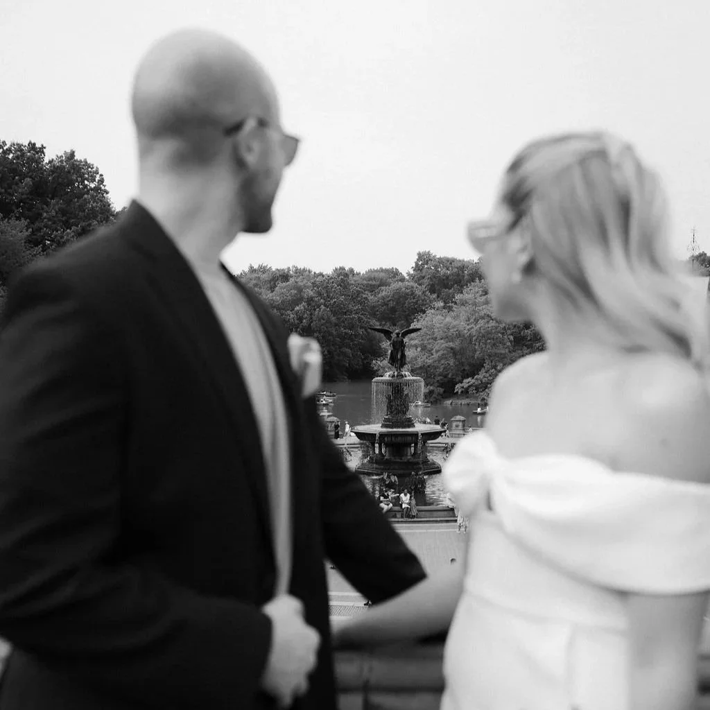 Black and white photo of Chloe and Sam holding hands in front of a Central Park fountain during their Cakewalk NYC elopement portraits.