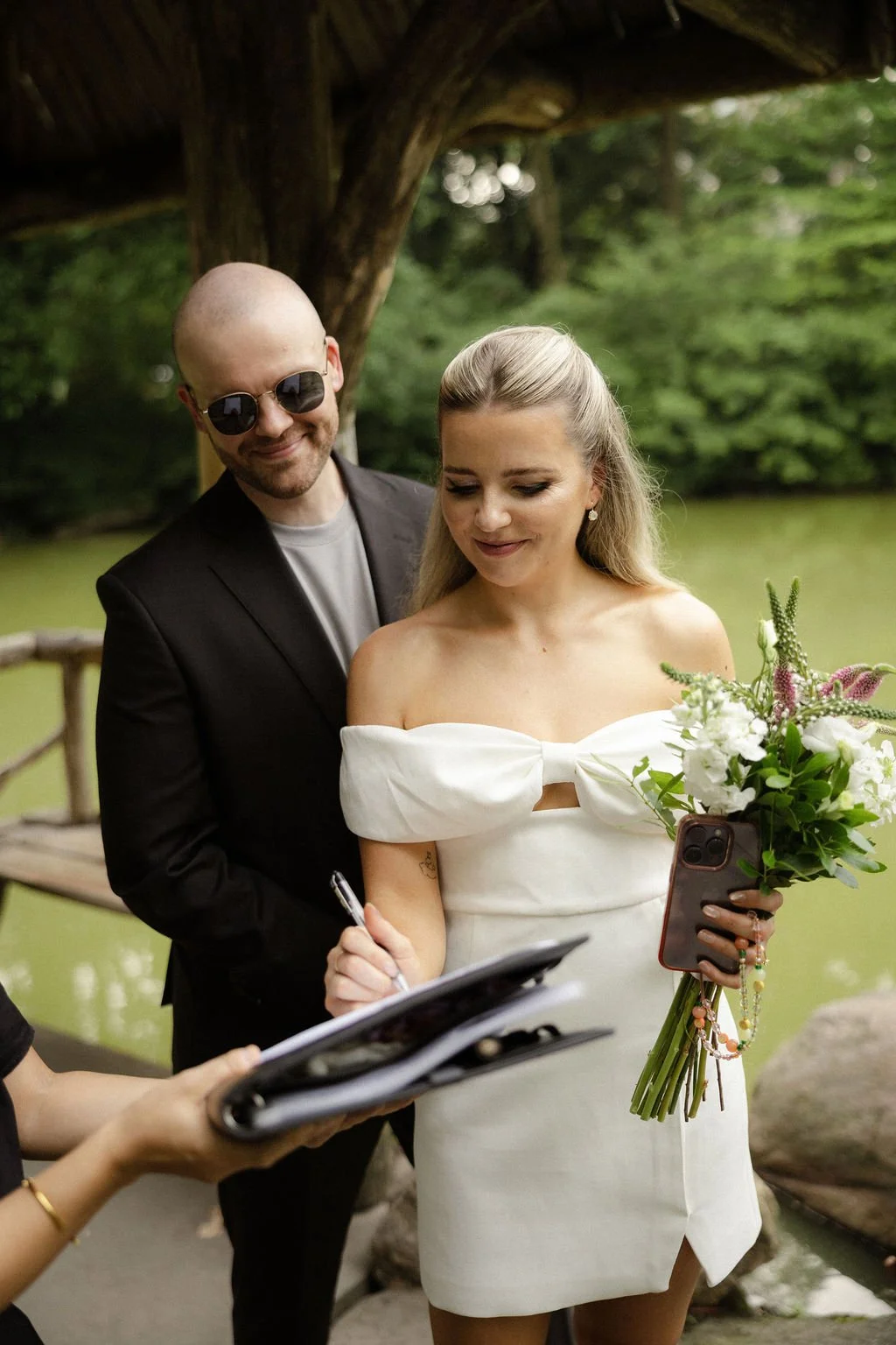 Bride and groom signing marriage license under the wooden lakeside pavilion at Wagner Cove after their Cakewalk NYC elopement.