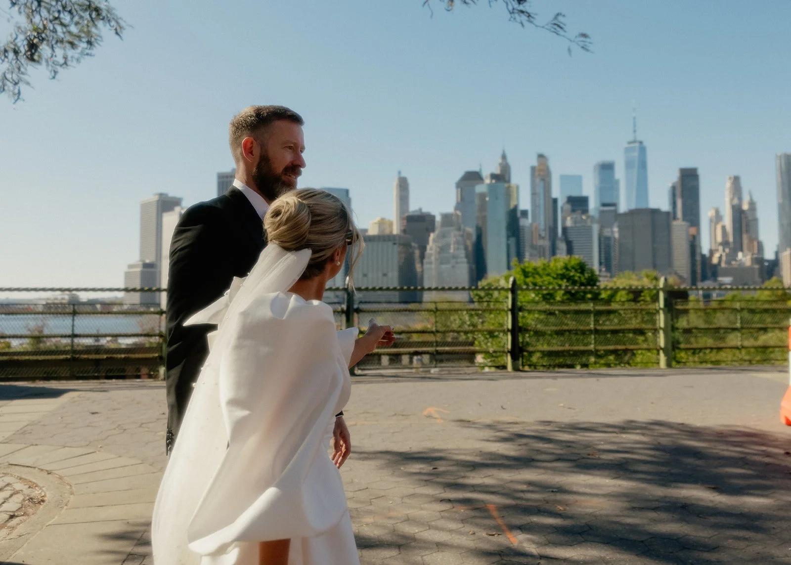 Bride and groom walking with the water and the Manhattan skyline in the background.