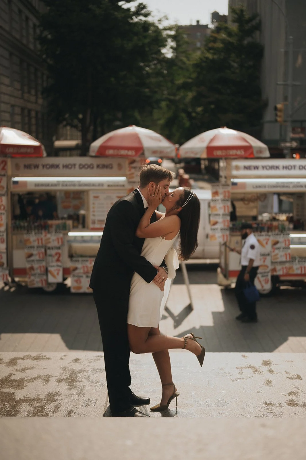 Kayla and Zach sharing a kiss at the base of the Met steps with classic New York hot dog carts in the background.
