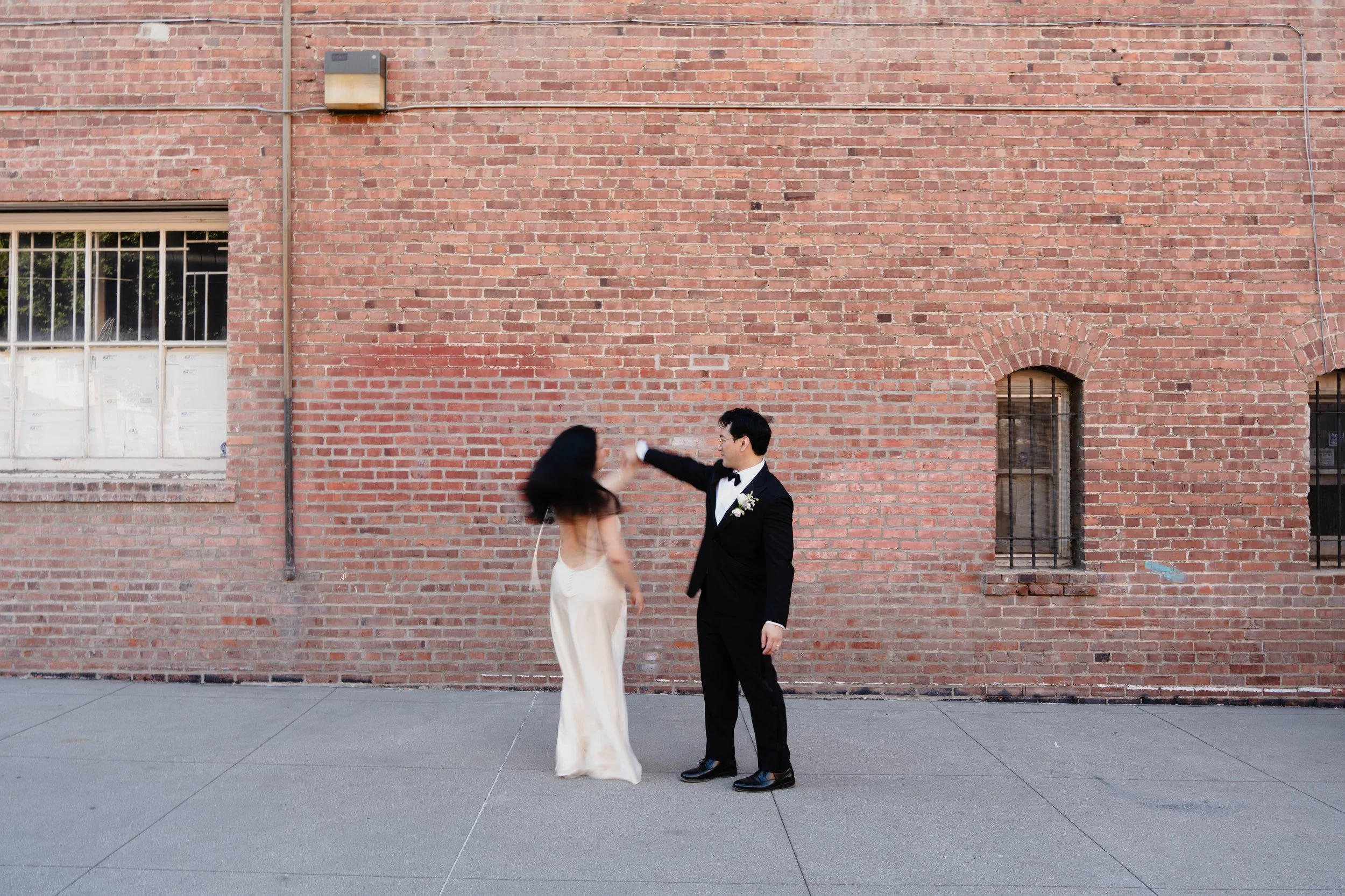 Groom twirling bride in front of a brick wall alleyway in Old Pasadena after their Cakewalk elopement.