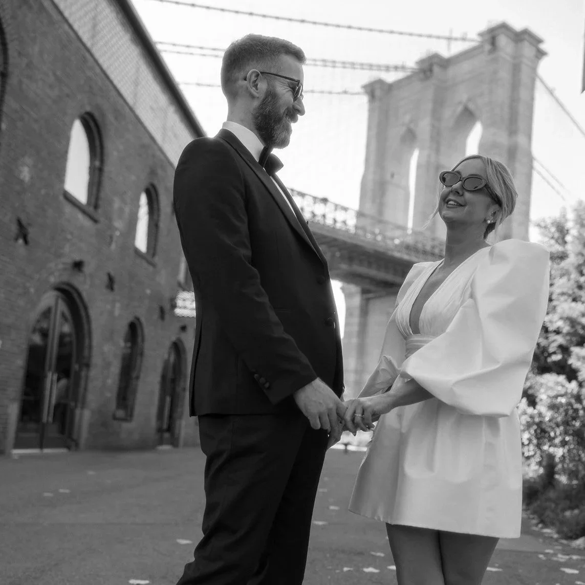 Couple in formal attire holding hands at the Brooklyn Bridge after their NYC elopement with Cakewalk